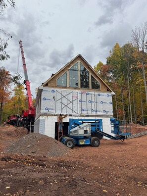 A house under construction with a large crane and construction vehicles. - Lake Gogebic Chalet at Cabin Creek (MARENISCO)