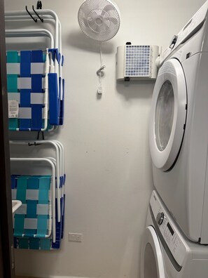 A laundry room with a stacked washer and dryer, a wall-mounted fan, and blue and white laundry baskets. - Little Corner of Paradise Sleeps 6, 2 Bath, 2 Room (Rincon)