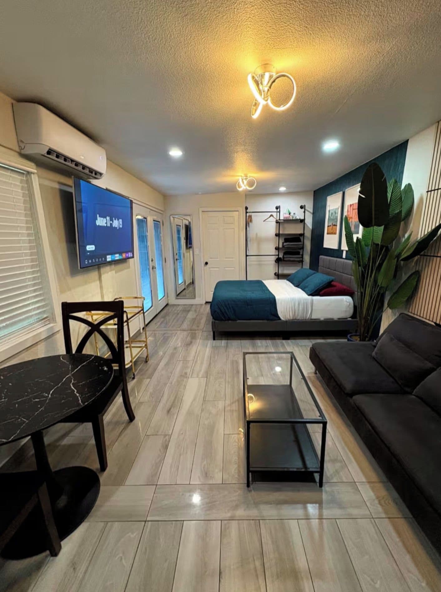 A modern living room with a flat-screen TV, a sofa, a coffee table, and a bed with a blue and white bedspread.