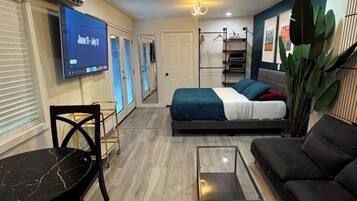 A modern living room with a flat-screen TV, a sofa, a coffee table, and a bed with a blue and white bedspread.