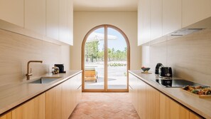 Eine moderne Küche mit Holzschränken, einer zentralen Kochinsel und Blick durch eine Rundbogenöffnung in einen Außenbereich.
