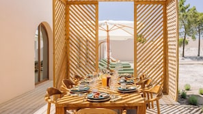 Ein Essbereich im Freien mit einer Holz-Pergola, einem gedeckten Tisch und Blick auf den Strand.