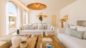 Un saló modern amb un sofà gran, una taula de centre i una taula de menjador. Hi ha un finestral gran amb cortines, una làmpada penjant i una obra d'art penjada a la paret.