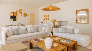 Een moderne woonkamer met twee witte banken, een houten salontafel en een hangende rotanlamp.