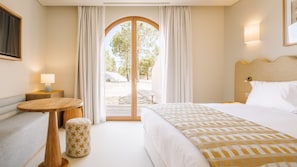A hotel room with a bed, a small table, a sofa, and a view through a glass door to an outdoor area. - Ando Living - Comporta Villas - Villa 3 (Carvalhal)