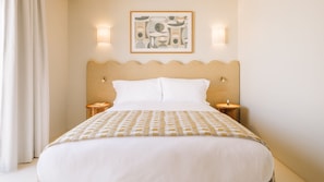 Une chambre d’hôtel comprenant un lit, deux tables de chevet, un luminaire fixé au mur et une œuvre d’art encadrée au-dessus du lit.