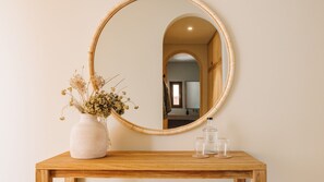 Een houten console tafel met een ronde spiegel, een vaas met gedroogde bloemen en twee glazen flessen.