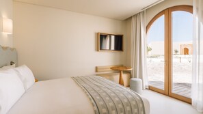 Ein Hotelzimmer mit einem großen Bett, einem kleinen Tisch, einem Fernseher und Blick auf die Wüste.