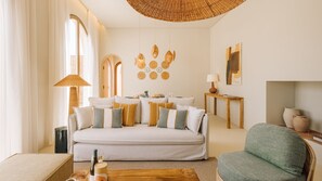 A modern living room with a sofa, armchairs, a coffee table, and a dining area with a table set for two. - Ando Living - Comporta Villas - Villa 9 (Carvalhal)