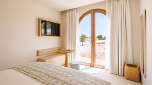 Una habitació d'hotel amb un llit, una taula petita, una televisió, una finestra amb cortines i vistes a l'exterior.