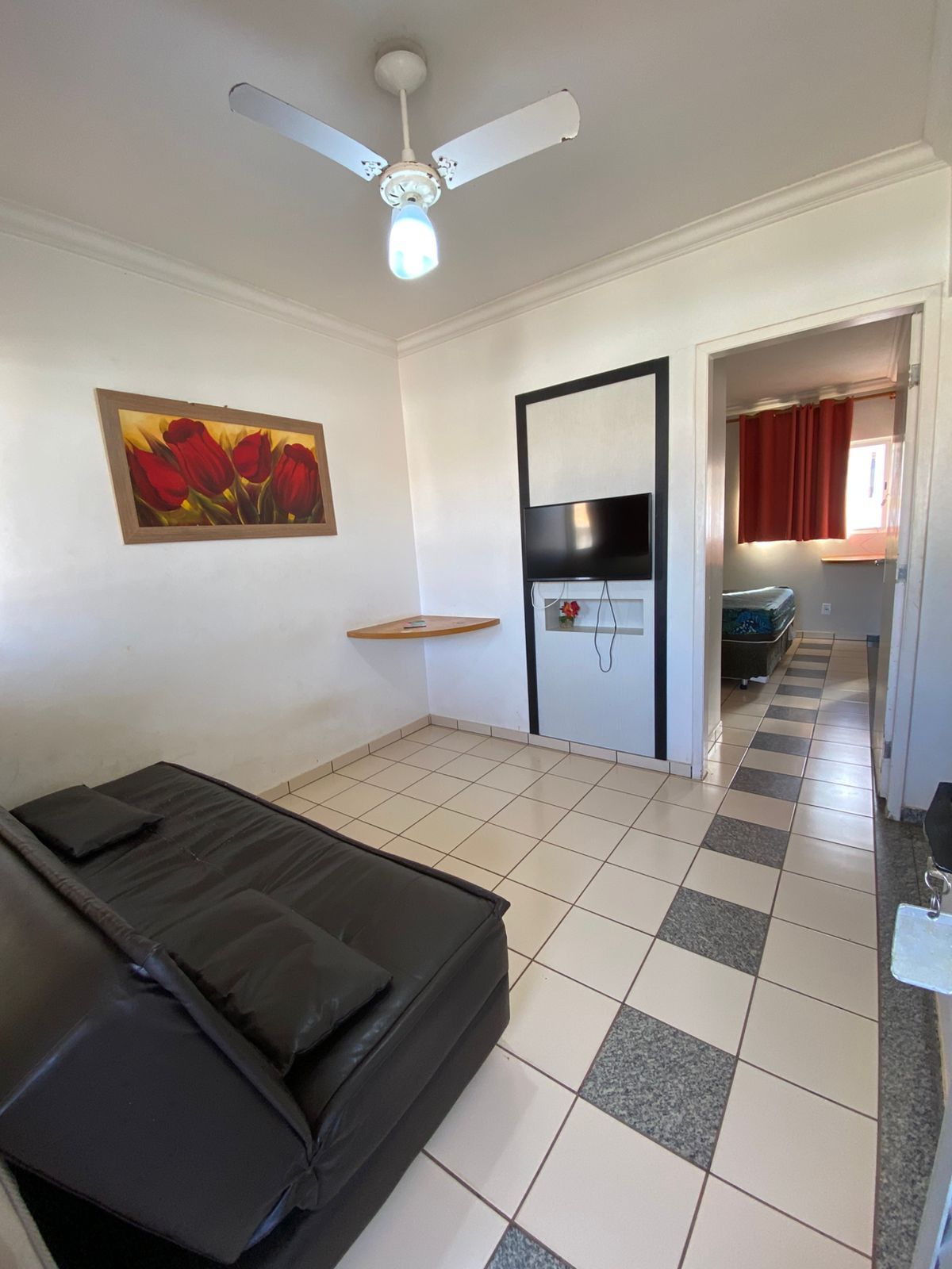 Une chambre avec un lit, un ventilateur de plafond, une télévision et un tableau au mur.
