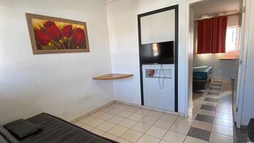 Une chambre avec un lit, un ventilateur de plafond, une télévision et un tableau au mur.