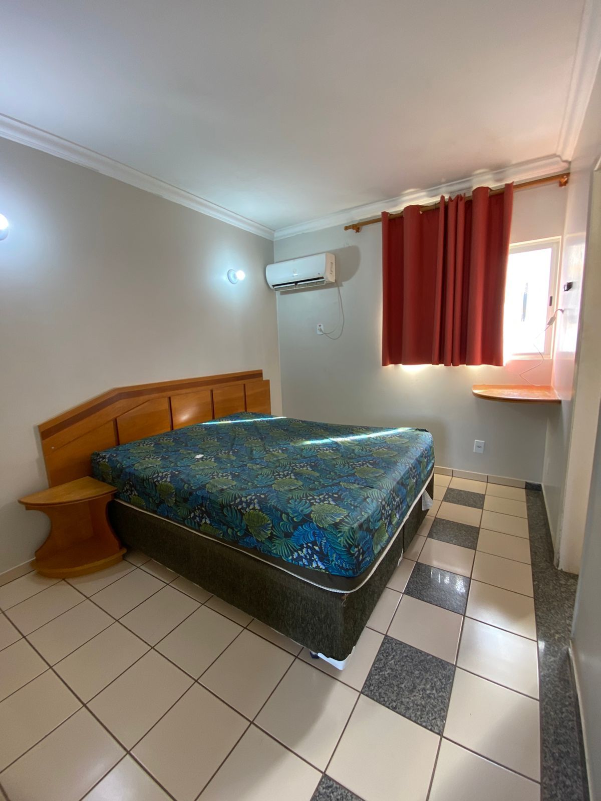 Un dormitorio con cama, mesita de noche, ventana con cortinas y aire acondicionado.
