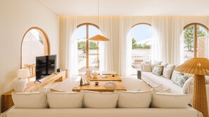 A spacious living room with a large sofa, a television, and a dining area. - Ando Living - Comporta Villas - Villa 11 (Carvalhal)