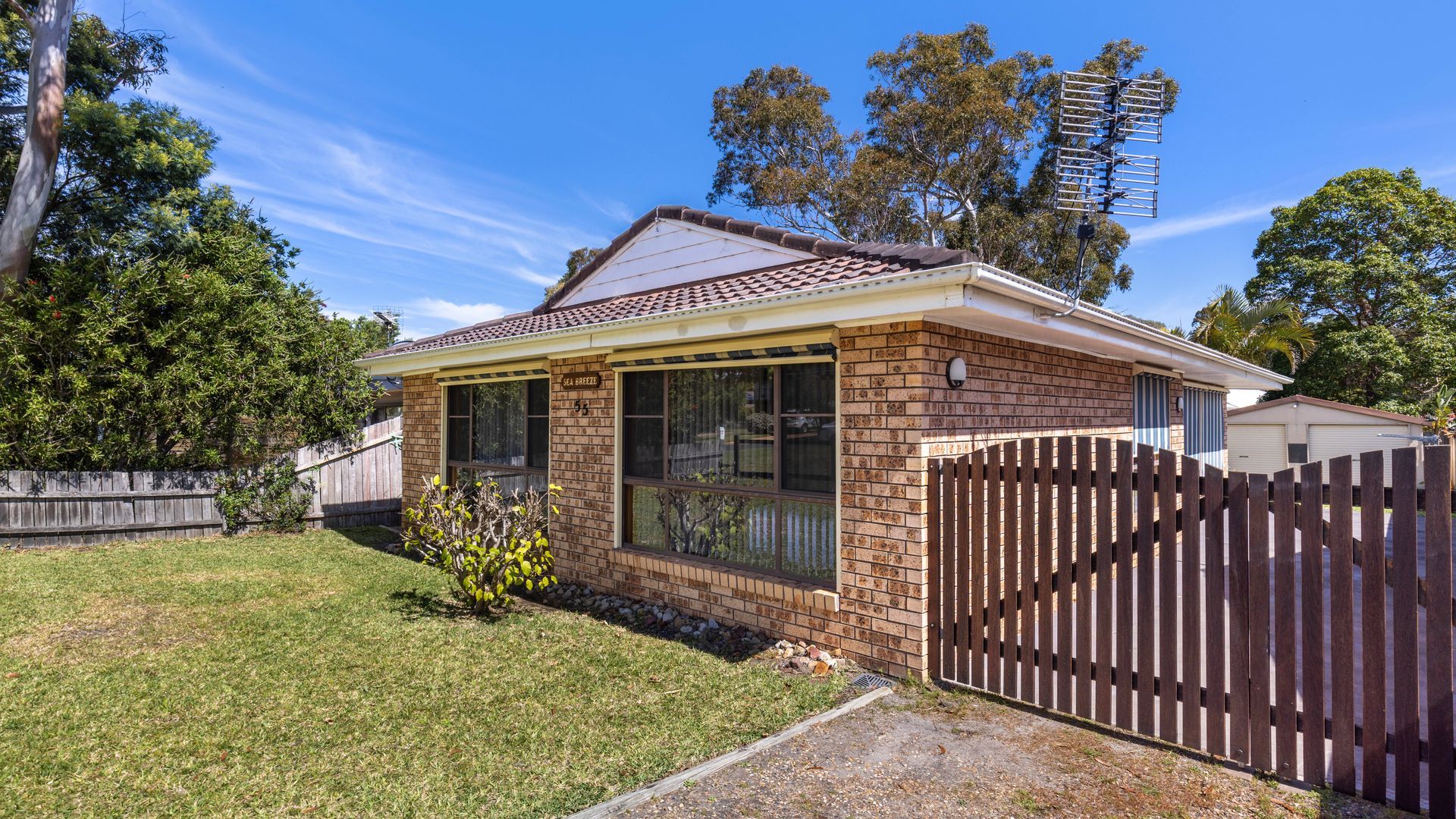 A single-story house with a brick exterior, a tiled roof, and a fenced backyard.