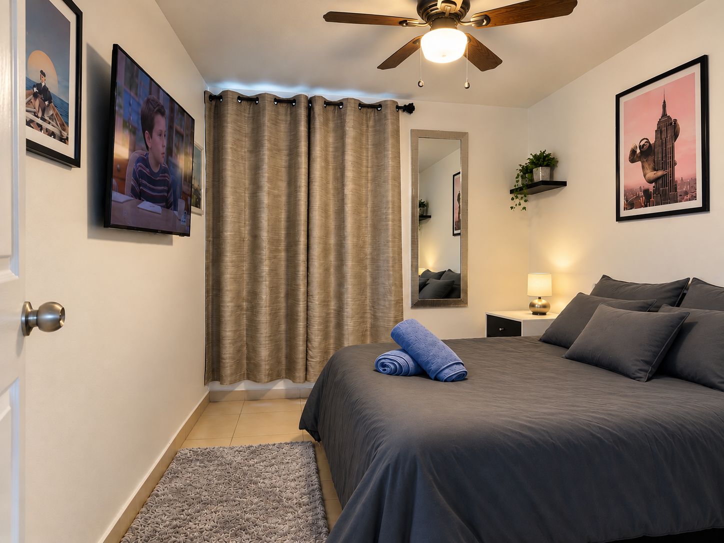 A bedroom with a bed, a ceiling fan, a mirror, and a nightstand.