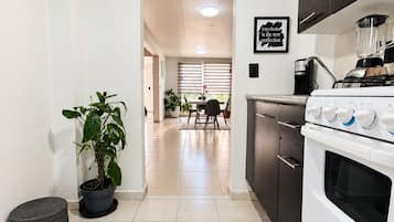 Een moderne keuken met een kookplaat, oven en aanrecht. Op de achtergrond is een eethoek met een tafel en stoelen.