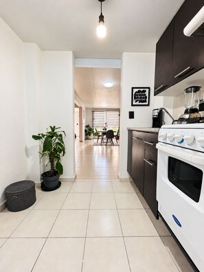 A modern kitchen with a stove, oven, and countertop. There is a dining area in the background with a table and chairs.