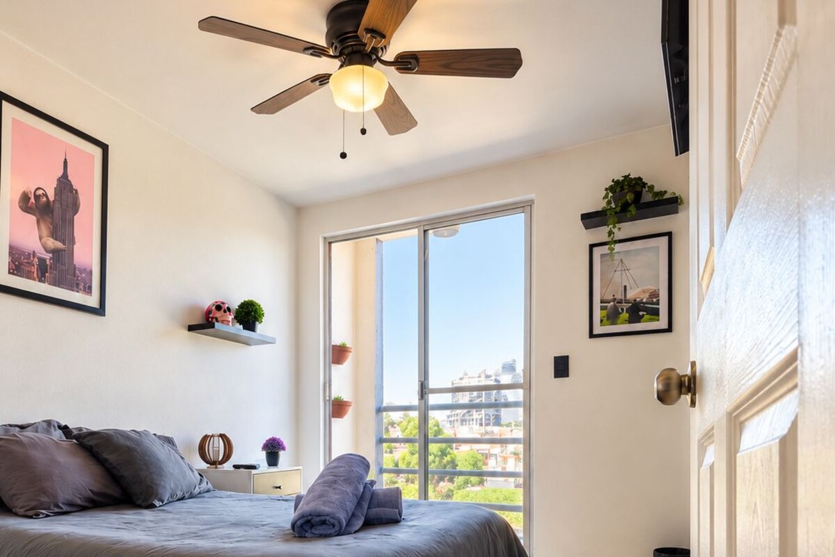 A bedroom with a bed, a ceiling fan, a window, and a door.