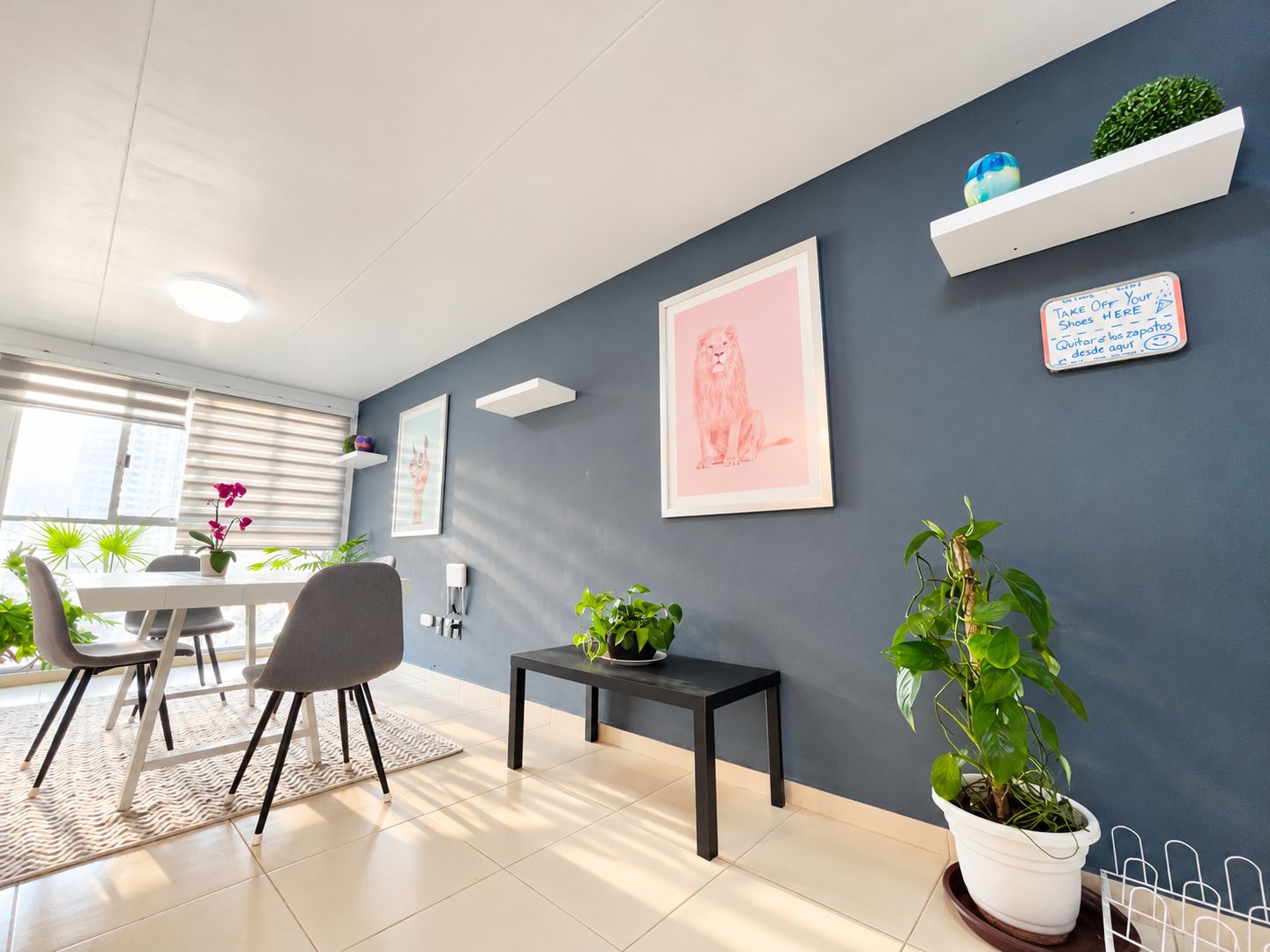 A modern living room with a dining area, featuring a grey sofa, a dining table, and potted plants.