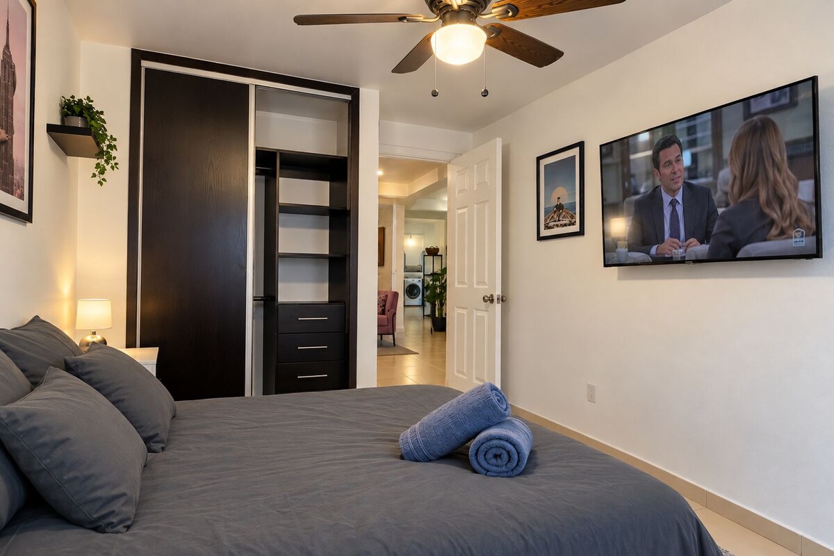 A bedroom with a bed, a ceiling fan, a TV, and a wardrobe.