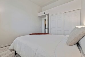 Quarto com cama, paredes brancas, porta branca e teto branco.