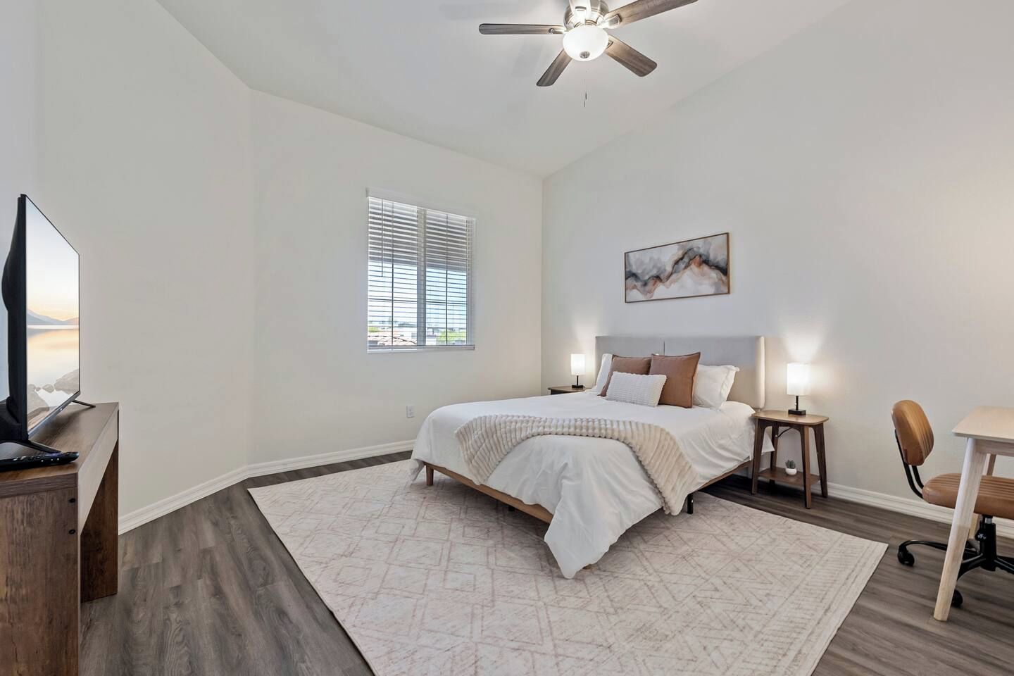 A bedroom with a bed, bedside tables, a desk, a chair, a television, and a ceiling fan.