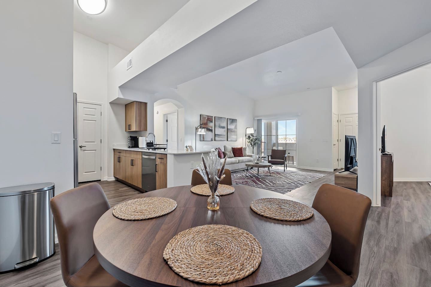 Une cuisine moderne avec des meubles en bois, un lave-vaisselle et un coin repas comprenant une table ronde et des sets de table en fibres tressées.