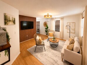 A modern living room with a flat-screen TV, a sofa, a coffee table, and a dining area with a chair and a plant. - Aroma Escape 🌴 Private Hot Tub • Near Beaches • Pet-Friendly (Bradenton)