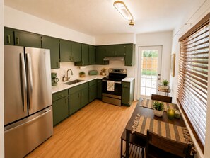 A modern kitchen with green cabinets, stainless steel appliances, and a wooden dining table. - Aroma Escape 🌴 Private Hot Tub • Near Beaches • Pet-Friendly (Bradenton)