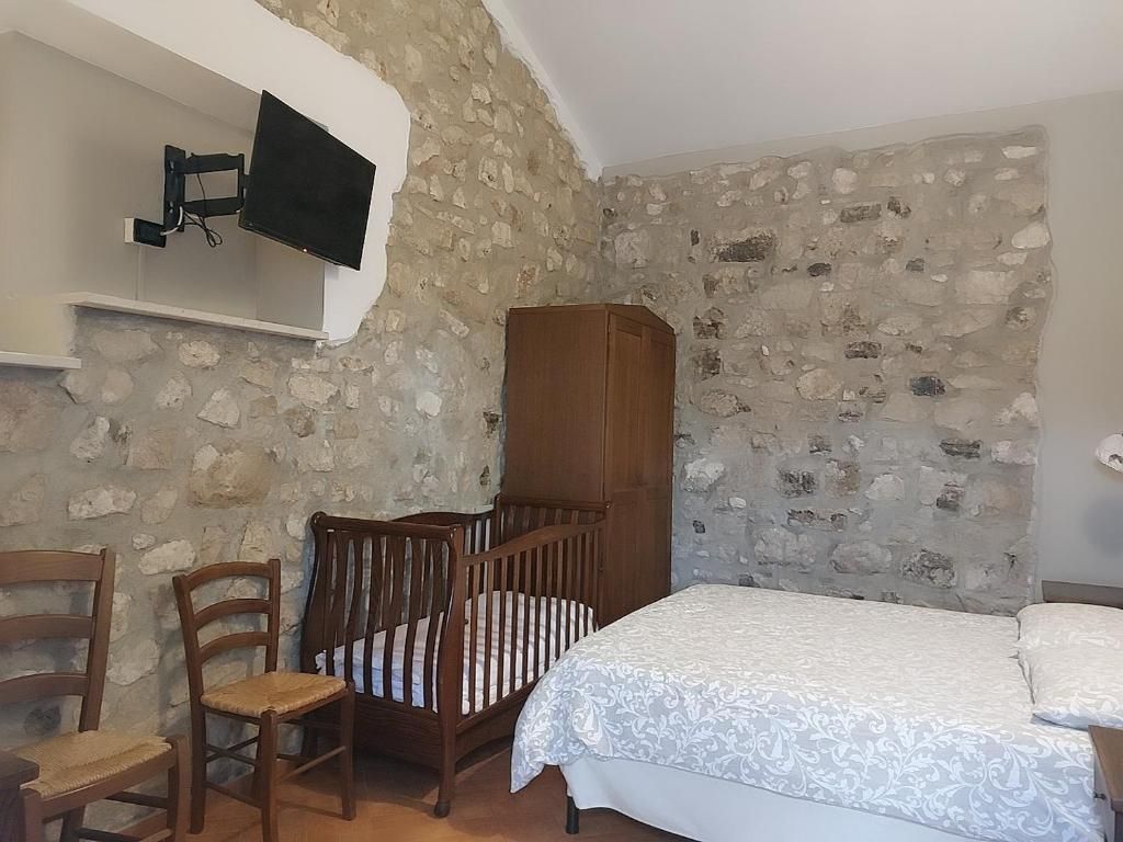 Ein Schlafzimmer mit einer Steinsäule, einem hölzernen Babybett, einem Bett mit gemustertem Überwurf, einem Holzschrank und einem angebrachten Fernseher.