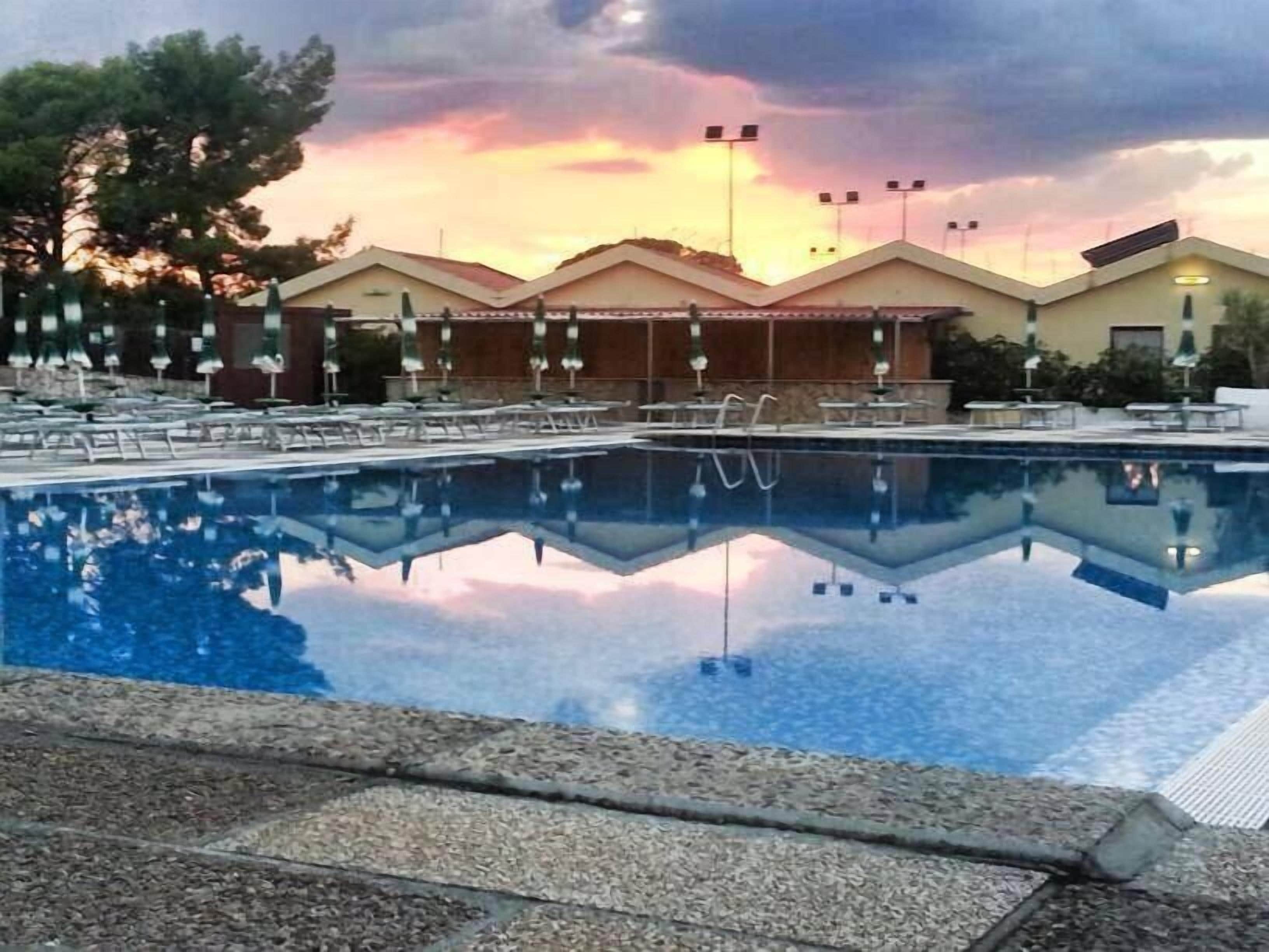 Ein Pool mit Liegestühlen und Sonnenschirmen, der ein Gebäude mit einem Ziegeldach widerspiegelt.