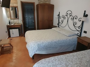 A bedroom with a bed, a wooden wardrobe, a desk with a chair, and a bathroom with a shower.