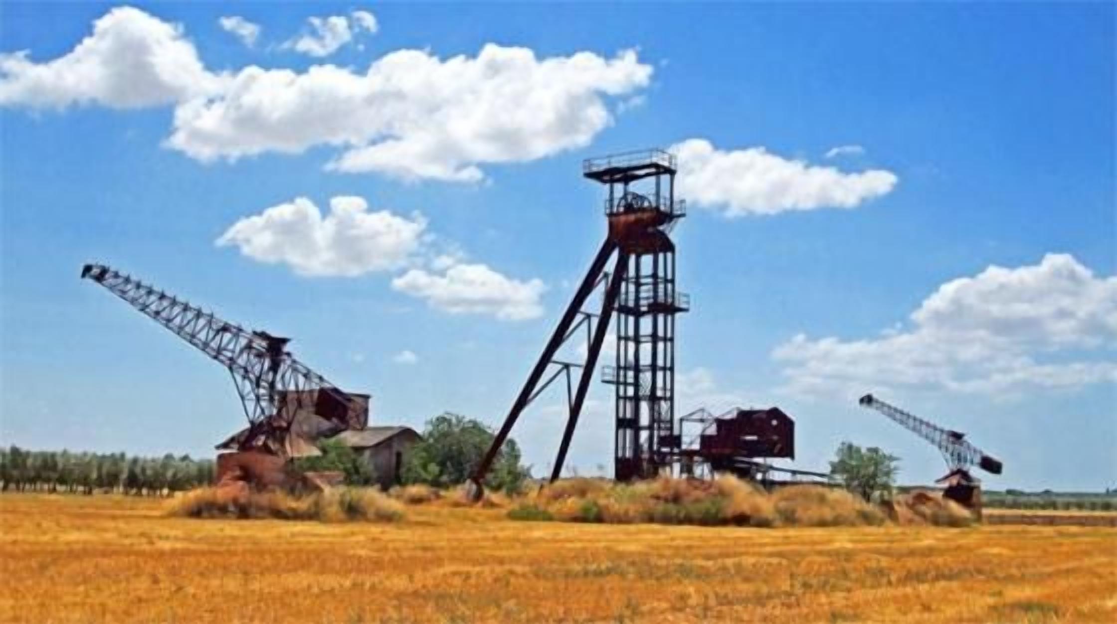 A large industrial structure with a tall tower and two cranes in a field.