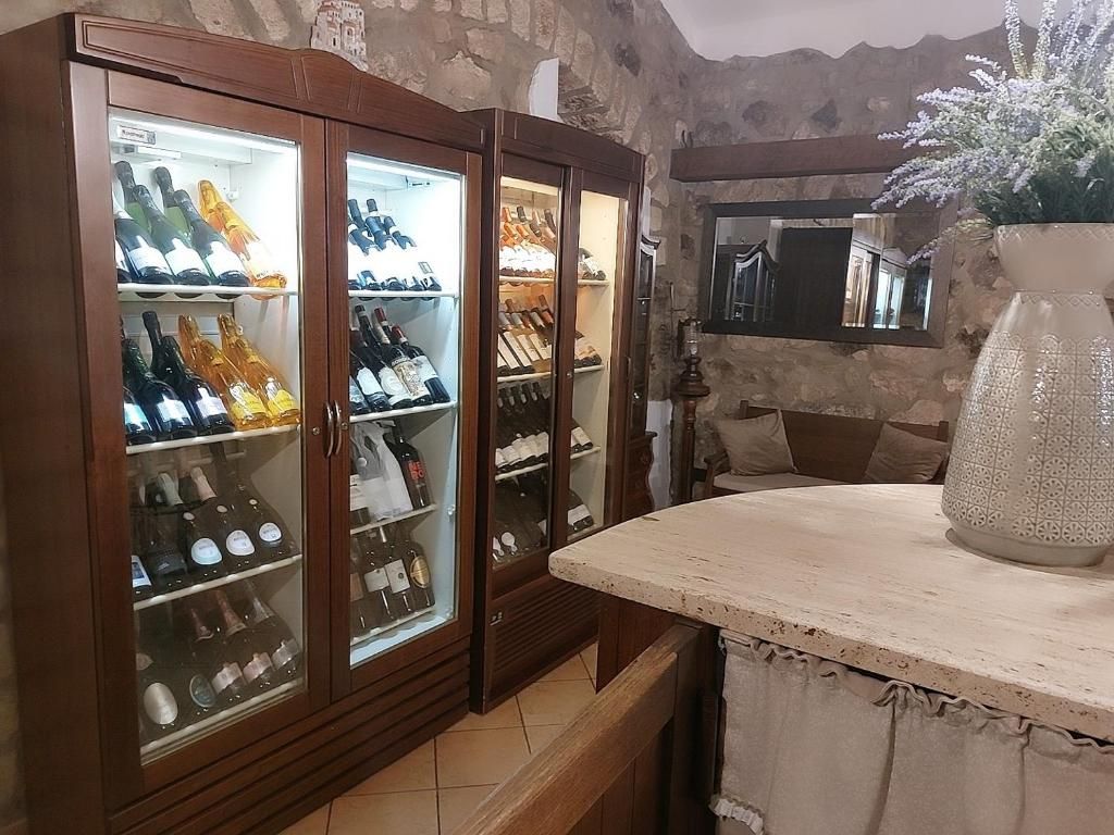 Zona de bar con un mueble de madera que contiene botellas, un gran jarrón decorativo y un fondo de pared de piedra.
