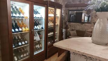 Zona de bar con un mueble de madera que contiene botellas, un gran jarrón decorativo y un fondo de pared de piedra.