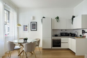 Eine moderne Küche mit weißen Schränken, einem runden Glastisch und einem Essbereich mit Stühlen.