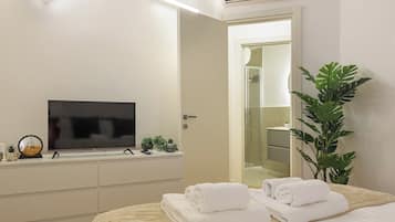 A hotel room with a bed, a television, a bathroom with a shower, and a potted plant.