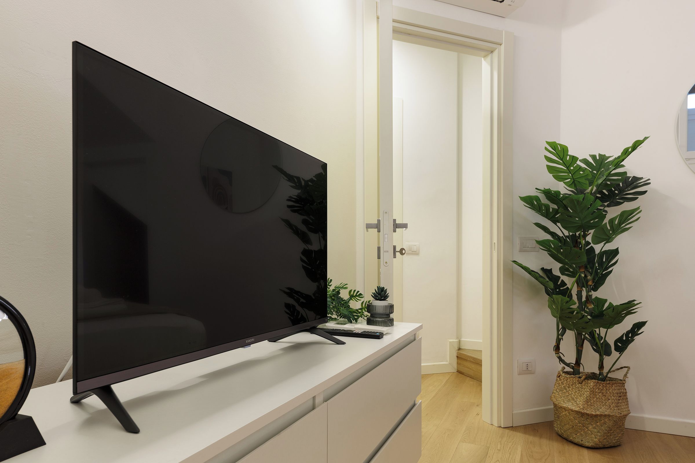 A flat-screen TV on a white dresser in a room with a door and a potted plant.