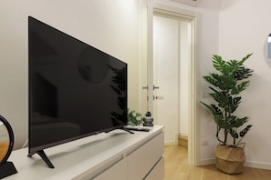 A flat-screen TV on a white dresser in a room with a door and a potted plant. - Executive Suite Nirone 8 (Milano)