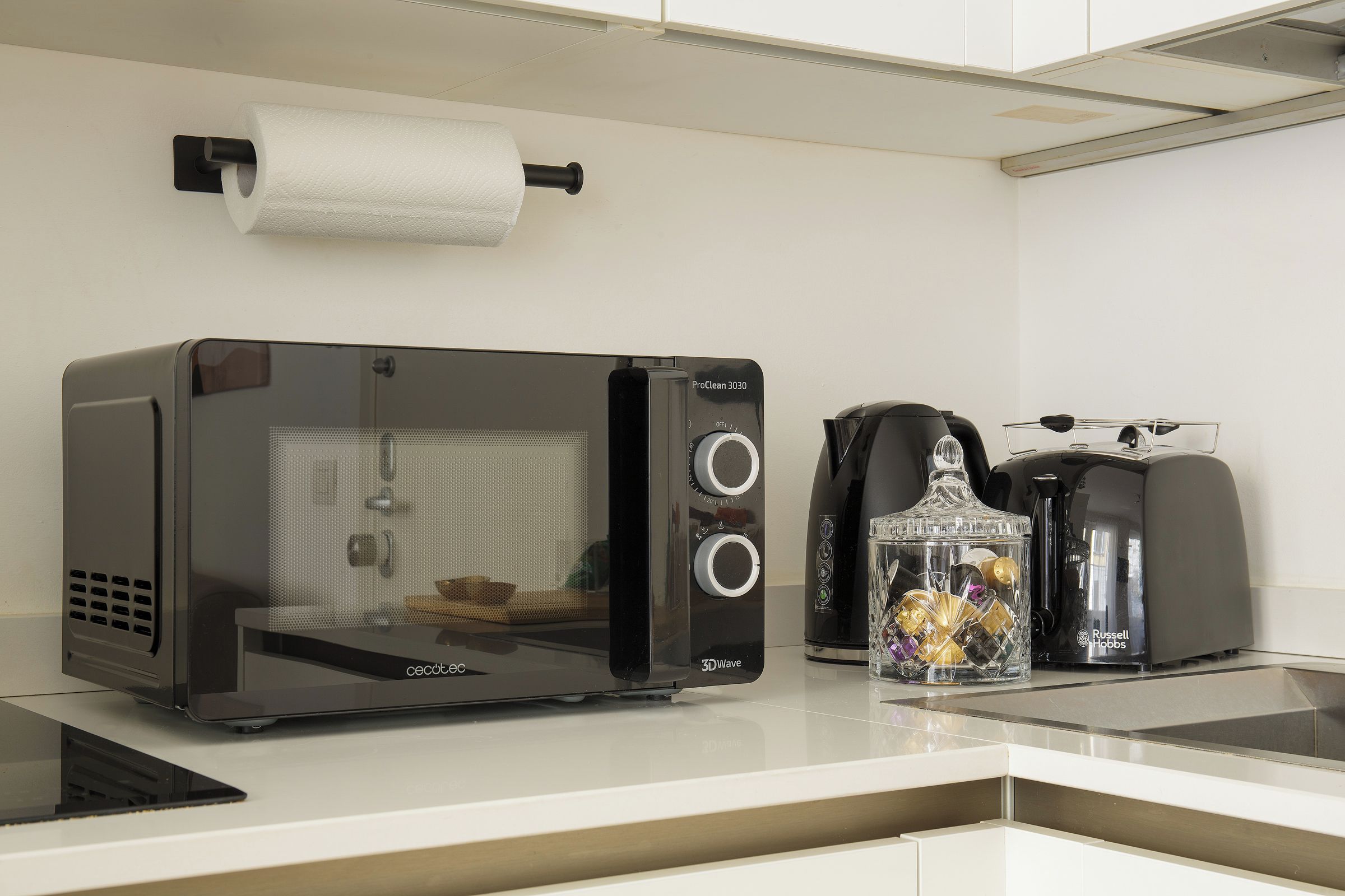 Una kitchenette con horno tostador 3DWave, cafetera y tarro de vidrio con objetos decorativos.