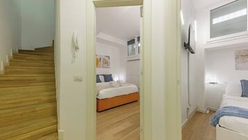 A hotel room with a wooden staircase, a bed with white bedding, a bedside table, and a wall-mounted TV.