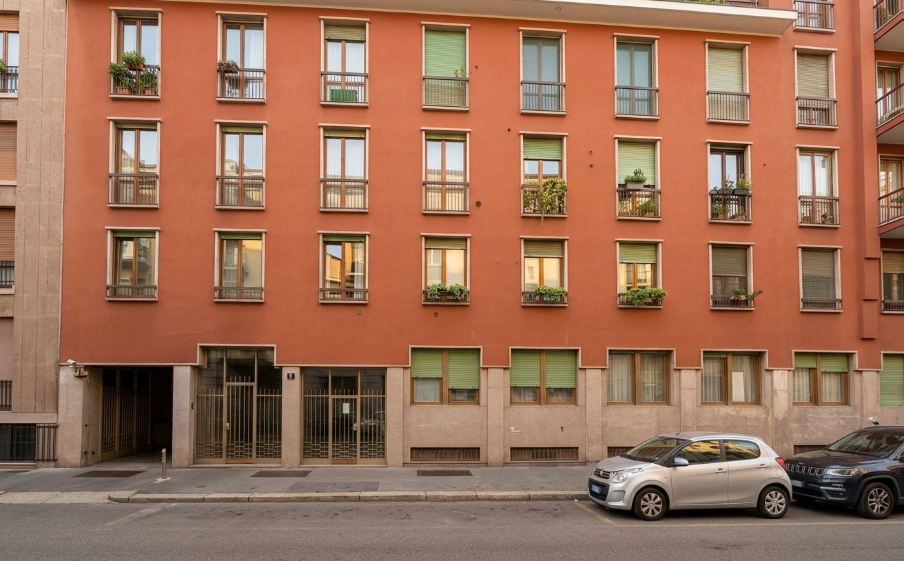 Un edificio de varios pisos con fachada roja, múltiples balcones con plantas y un acceso con portón.