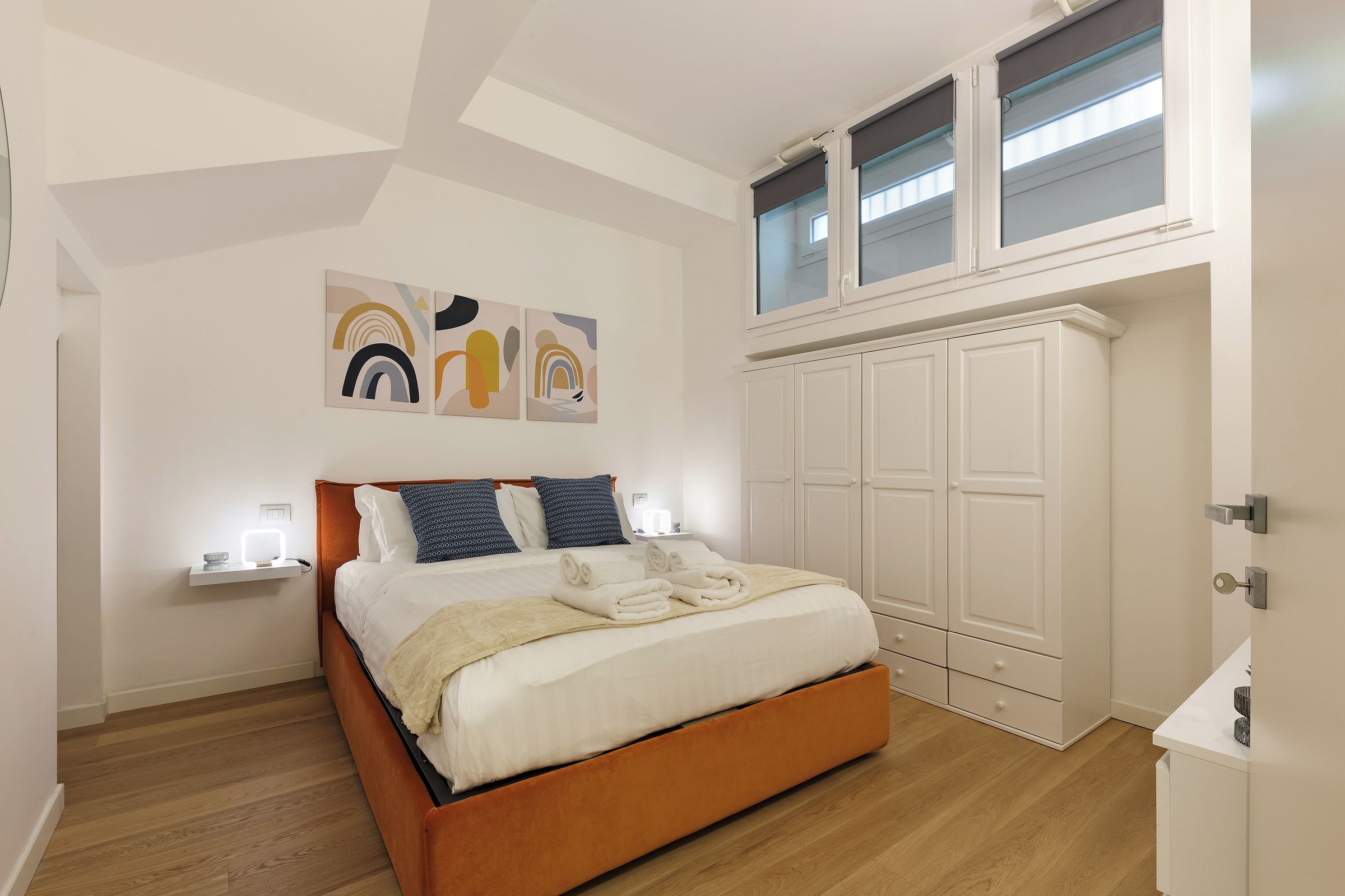 Un dormitorio con cama, mesitas de noche, armario y una obra de arte en la pared.