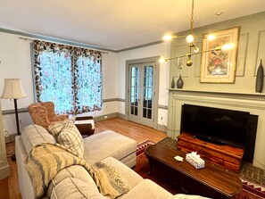 A living room with a sofa set, a television, a fireplace, and a patterned window. - Camden at Monticello (Salisbury)