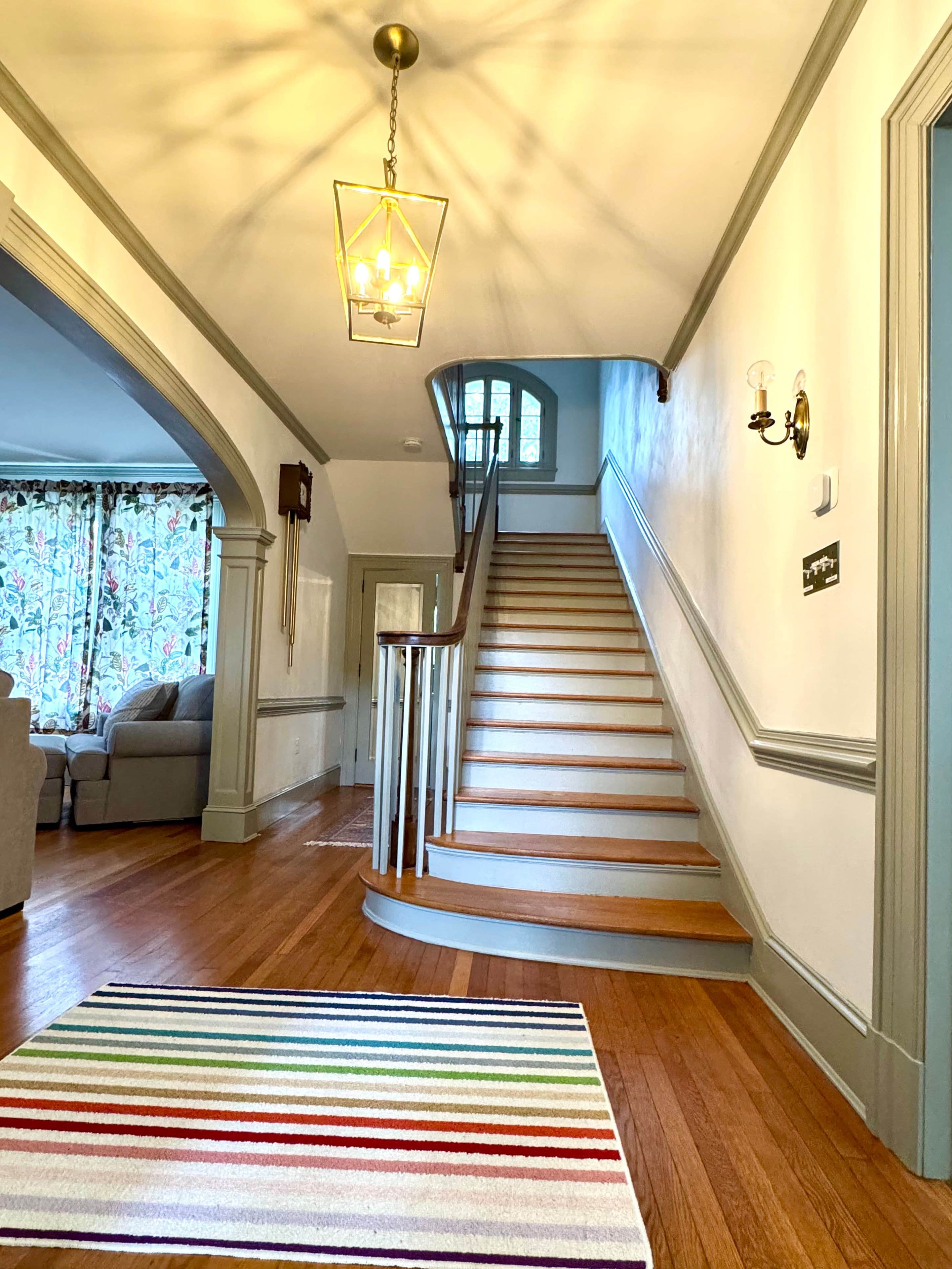Un escalier avec des marches en bois menant à un palier, un luminaire suspendu et un tapis à rayures sur le sol.