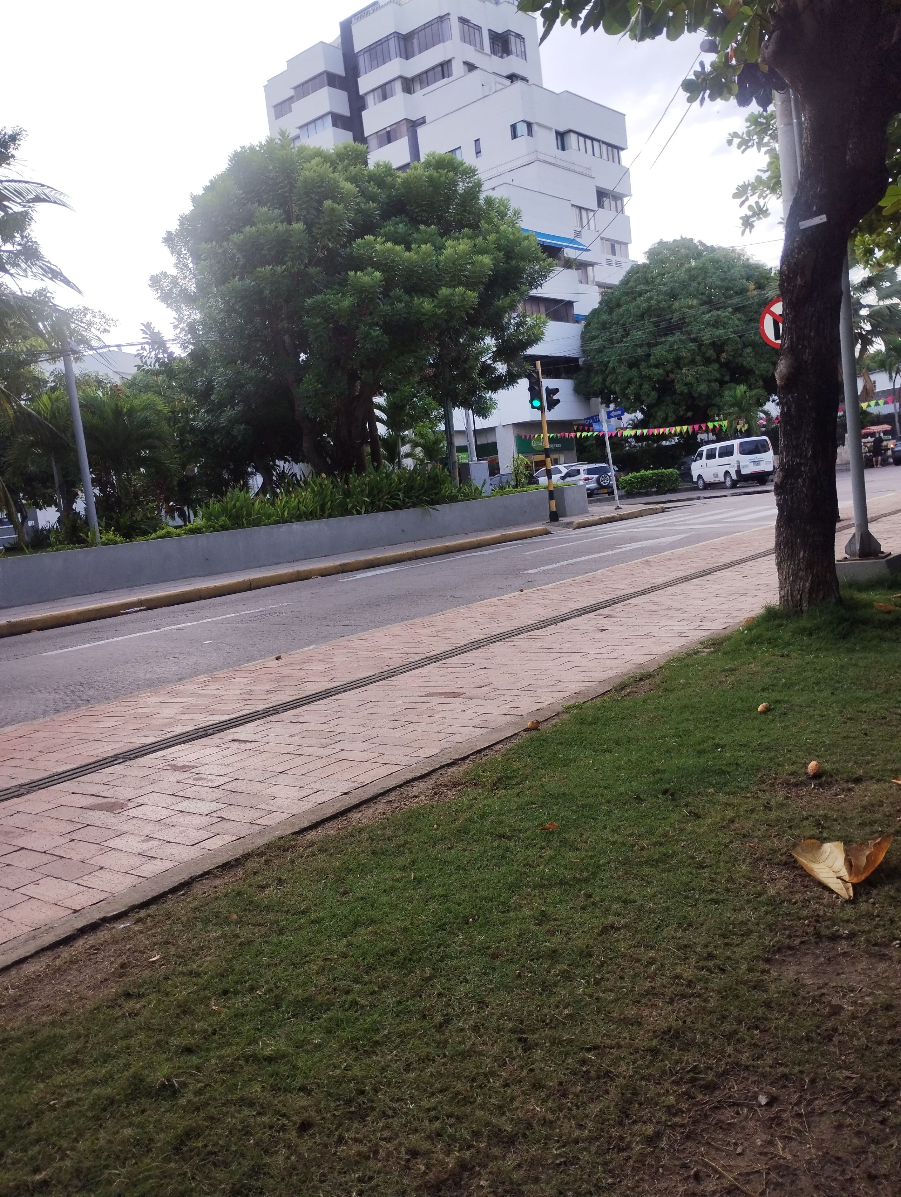 A paved sidewalk adjacent to a road with a traffic light, a white van, and a building in the background.