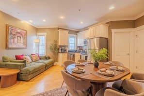 A spacious living room with a green sofa, a dining table set for six, and a kitchen in the background. - Cambridge Cozy Home ,3bedroom/2bath ,Sleeps 8 (Cambridge)