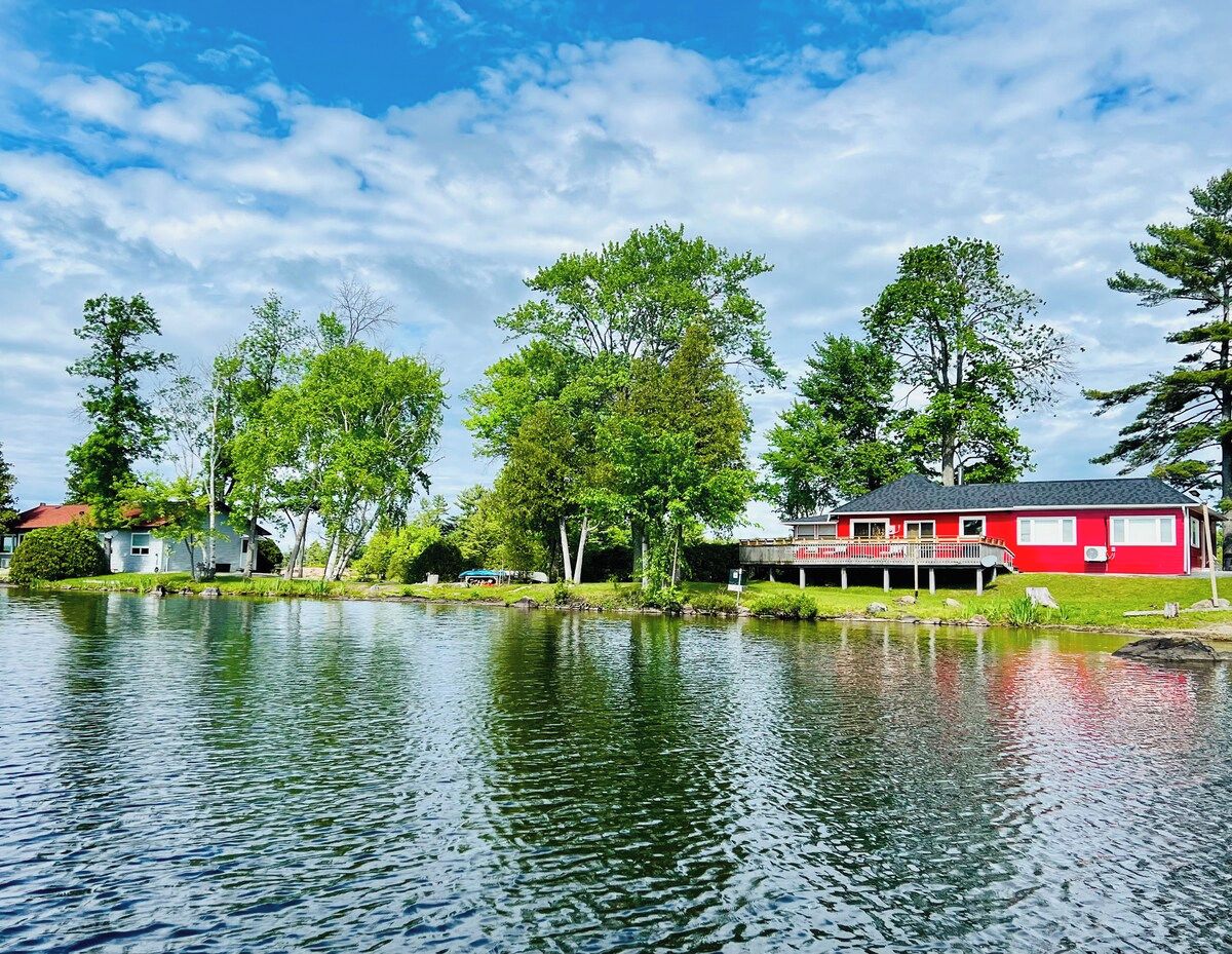 A lakeside property with a red building, a dock, and surrounding greenery.