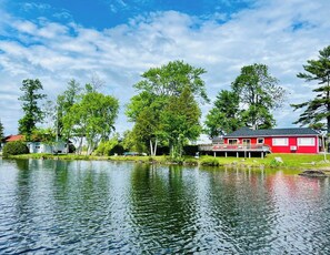 Una propiedad junto al lago con un edificio rojo, un muelle y vegetación circundante.